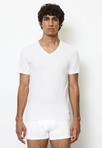 Witte T-shirt met korte mouwen en V-hals, gemaakt van een gladde stof en met een aansluitend ontwerp. Het is gecombineerd met witte boxershorts, gezien vanuit een frontaal perspectief tegen een effen achtergrond.