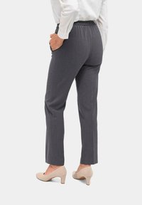 Grijze elastische broek met een rechte pijp, voorzien van zijzakken en een gladde textuur, gecombineerd met lichtbeige hakken.