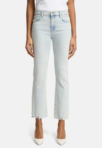 Jeans in denim azzurro chiaro a gamba svasata con vita alta, orlo strappato e design a cinque tasche. Indossati con tacchi bianchi a punta.