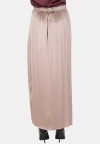 Gonna lunga beige chiaro con vita arricciata indossata con stivali neri con tacco alto e top scuro, vista da dietro senza motivo visibile.