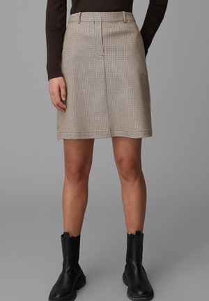 Beige houndstooth mini skirt yang terbuat dari kain tekstur, dilengkapi dengan lipatan depan dan loop sabuk, dipadukan dengan bot boots hitam setinggi pergelangan kaki.