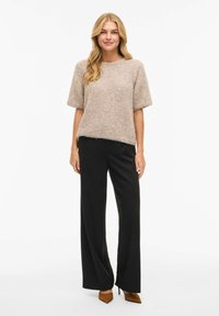 Beige, kortermet strikket topp med løs passform, kombinert med svarte bukser med vide ben og brune spisse høye hæler. Myk tekstur og casual design.