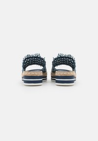 Blå vävda sandaler med en texturerad ovandel, espadrillastil i jute-mellansula och vit och marinrandig gummisula. Öppen baksida.