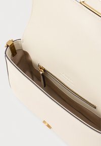 Ανοιχτό μπεζ δερμάτινη τσάντα χεριού με λεία υφή, που διαθέτει χρυσά αξεσουάρ, τσέπη με φερμουάρ και αντίθετο σκούρο περικάλυμμα.