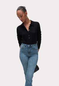 Camisa polo negra de manga larga con cuello abotonado, combinada con vaqueros de tiro alto de color azul claro y un pequeño bolso cruzado negro.