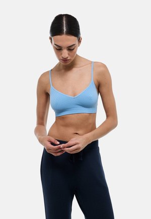 Bralette côtelé bleu clair avec de fines bretelles réglables, design en V et bords sans couture, porté avec un pantalon de jogging bleu marine.