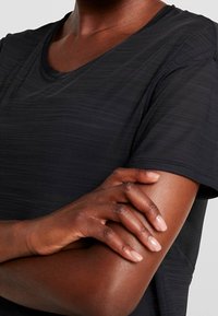 Black short-sleeve top featuring a textured fabric, round neckline, and subtle diagonal striping. Includes a mesh accent on the back.