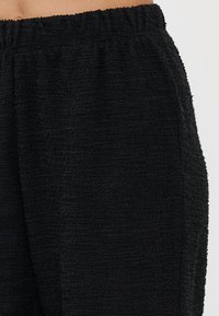 Sorte teksturerte bukser laget av myk stoff med elastisk midjebånd, med en litt løs passform og en fluffy utseende.