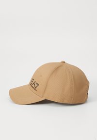 Tan cap made of smooth fabric, featuring a curved brim, stitched detailing, and a black EA logo on the front with an adjustable strap at the back.