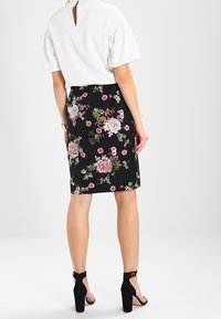 Svart blommig blyertskjol med rosa och vita blommor, kombinerad med en vit blus. Outfiten fulländas med svarta högklackade sandaler.