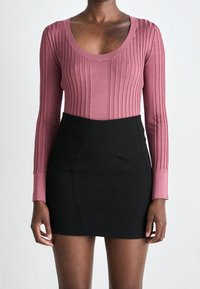 Langärmliges, geripptes Oberteil in staubigem Rosé, kombiniert mit einem hochgeschnittenen schwarzen Minirock. Sanfte Textur mit einer taillierten Silhouette.