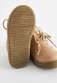 Bottines en suédine beige, à bout rond, doublées d'un matériau doux, avec fermeture à lacets et semelle en caoutchouc texturé avec des nervures.