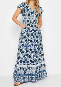 Blommig maxiklänning med blå och vita mönster, korta volangärmar, V-hals, elastisk midja och fickor. Utsmyckad med en spetskant.