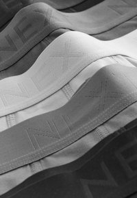 Bandas de tela en diferentes tonalidades de gris, con un patrón texturizado y marcadas con "NEX" en su superficie. Material suave y elástico.