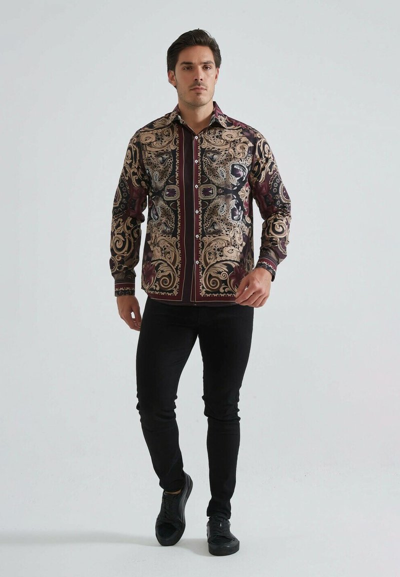 Chemise à manches longues avec un motif paisley dans des nuances de bordeaux et d'or, associée à un pantalon noir ajusté et des baskets.