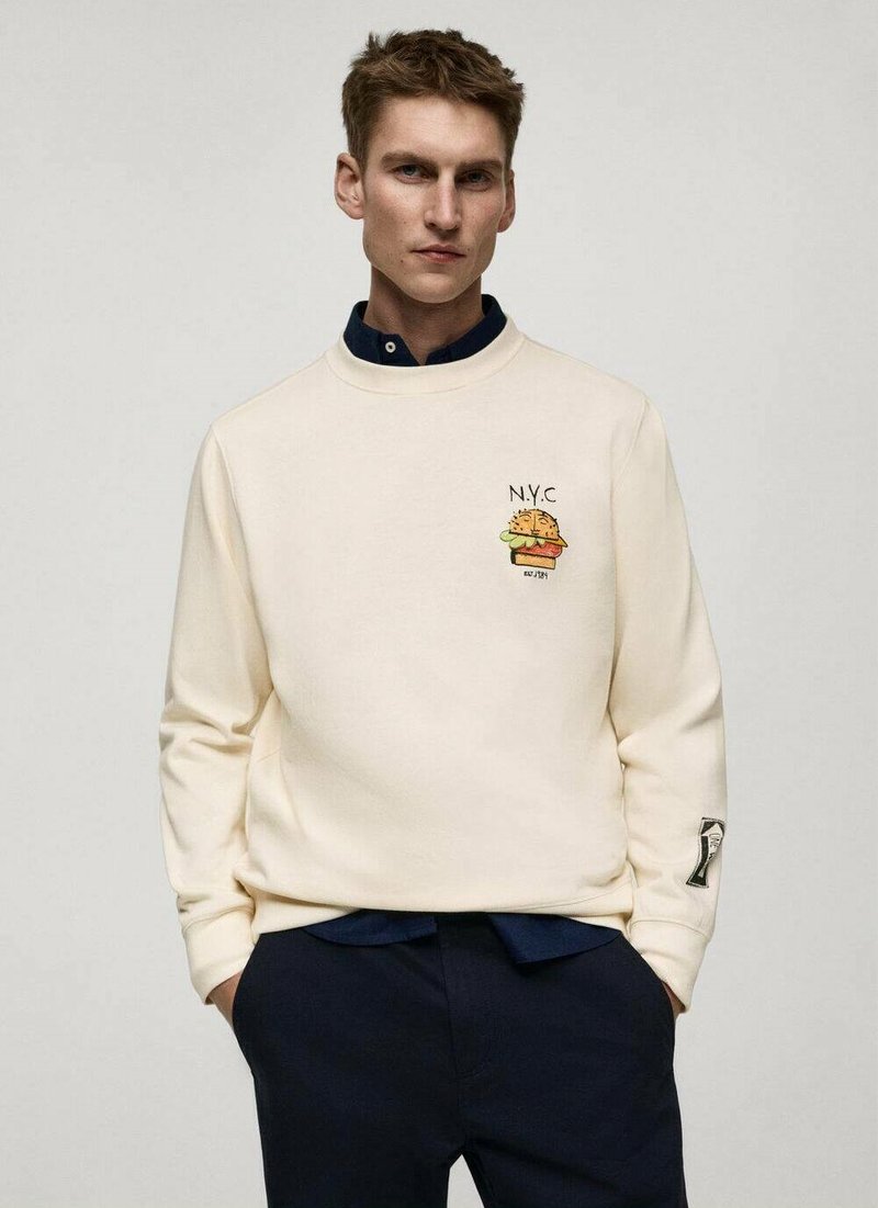 Felpa color crema con scollo rotondo, caratterizzata da un hamburger in stile cartone animato e ricamo "N.Y.C". Polsini a costine con un accento decorativo su una manica.