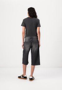 Gray t-shirt, cropped design; dark gray denim culottes with a faded texture; black and white sneakers with a textured sole.