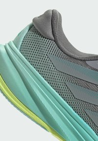 Scarpa da ginnastica grigia con una tomaia in rete traspirante, accenti azzurri, una suola texturizzata e un collare imbottito per il massimo comfort.