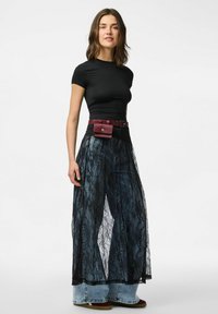 Top aderente nero a maniche corte, sovrapposto a una gonna in pizzo nero trasparente. Pantaloni larghi in denim sotto, con una cintura in pelle borgogna e una pochette.