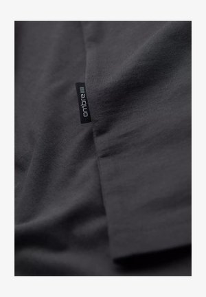 T-shirt en tissu gris foncé avec une texture lisse, arborant une petite étiquette noire "ombre" sur l'ourlet latéral. Design simple et classique.