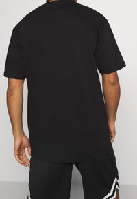 Svart kortärmad t-shirt, avslappnad passform, rund hals, slät bomullstextur, visad från ryggen, ihopparad med svarta shorts med vita accenter.