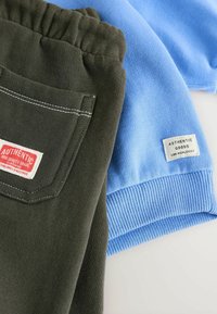 Groene sweats met witte stiksels en een achterzak, gecombineerd met een lichtblauwe trui met geribde manchetten en een label.