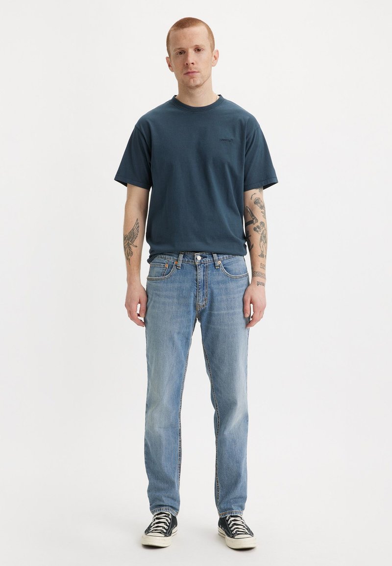 T-shirt en coton bleu marine avec un col rond, associé à un jean droit bleu clair et des baskets noires avec des accents blancs.