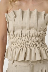 Haut beige sans bretelles avec une taille froncée, présentant des plis verticaux et un ourlet à volants, fabriqué en tissu texturé.