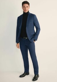 Granatowy garnitur w kratę o dopasowanym kroju, zestawiony z czarnym golfem. Gładki materiał, elegancka tekstura i wypolerowane czarne buty.