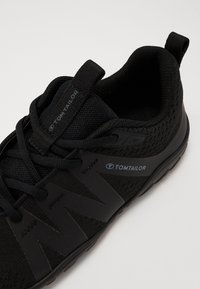 Svart sportssko med mesh-overdel, gummisåle og merkevarer, med et elegant design og teksturert overflate for grep.