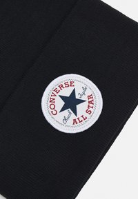 Tessuto nero con una toppa rotonda bianca con il testo rosso "CONVERSE" e "ALL STAR", una stella blu al centro e dettagli di cucitura nera.