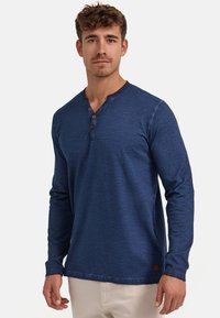Marineblaues Langarmhemd mit Henley-Ausschnitt, Holzknöpfen, weichem Stoff und leicht melierter Optik. Lässige Passform mit geradem Saum.