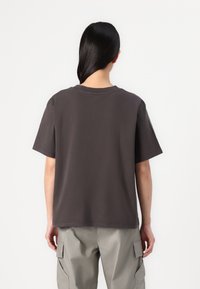 Grå bomuld t-shirt med en afslappet pasform, korte ærmer og rund halsudskæring, båret af en person i lyse cargo bukser.