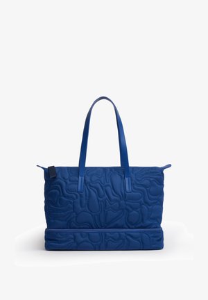 Blå quiltet tote taske med to håndtag og et separat lynlåslomme i bunden, vist mod en hvid baggrund.
