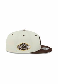 Casquette de baseball beige et marron avec un patch de logo du 50ème anniversaire pour 1969-2019 sur le côté et une visière plate.