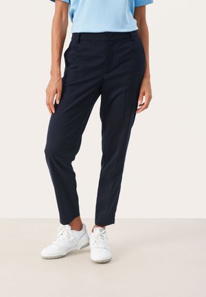 Pantaloni sartoriali blu marine con gamba dritta, caratterizzati da pieghe frontali e una vestibilità slim, abbinati a sneakers bianche e una maglietta azzurro chiaro.