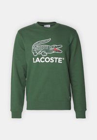 Zelená mikina vyrobená z bavlněné směsi, s bílým logem Lacoste a grafikou krokodýla. Hladké manžety a lem, klasický design s kulatým výstřihem.