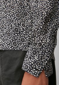 Camicia a fantasia floreale scura con un design in bianco e nero, dotata di polsini con bottoni e un texture di tessuto morbido. Dettaglio ravvicinato della manica.