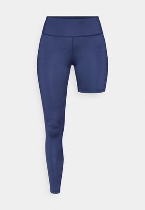 Granatowe legginsy z wysokim pasem, o gładkiej fakturze i krótszym kroju nogawki po prawej stronie. Bez widocznych elementów metalowych ani wzorów.