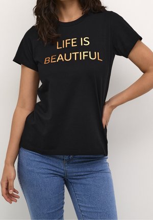 Kobieta ubrana w czarną koszulkę z złotym napisem "LIFE IS BEAUTIFUL" w połączeniu z niebieskimi dżinsami, pozująca na jednolitym białym tle.