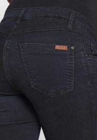 Jeans de ganga de lavagem escura com um design ajustado, bolsos traseiros distintos, costura mínima e um rótulo de couro na cintura.