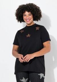 Sort kortærmet t-shirt med høj hals, prydet med brune mesh-stjerne-accenter på forsiden. Bæres med mørk denim jeans.