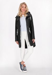 Czarny wodoodporny płaszcz z kapturem i białymi sznurkami, połączony z niebieską i białą paskowaną bluzką, białymi spodniami i niebieskimi trampkami.