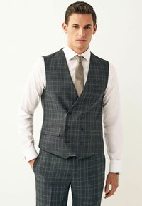 Gråternet vest med dobbeltrækkede design, der har justerbare taljebånd, båret over en hvid skjorte og suppleret med et mønstret slips.