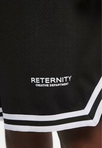 Svarte sportsshorts laget av teksturert stoff, med hvite detaljer og logo-tekst: "RETERNITY CREATIVE DEPARTMENT" brodert på siden.
