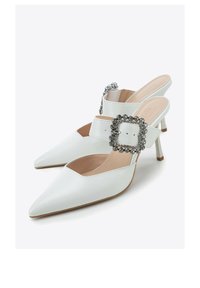 Bottes slingback blanches en cuir, avec embouts pointus, boucle décorative avec pierres, et talons carrés de 5 cm, présentant une texture lisse et un design épuré.