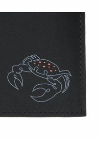 Coin en tissu noir avec un bord cousu mettant en avant un contour minimaliste de crabe avec des taches orange sur sa carapace.