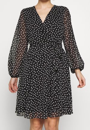 Czarna sukienka kopertowa w białe groszki, z przezroczystymi długimi rękawami i wiązanym paskiem w talii, o długości sięgającej połowy uda.