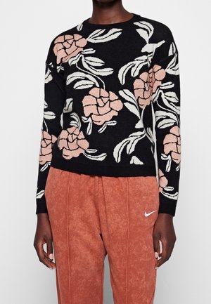 Svart tröja med vit och rosa blommönster, rund hals och lång ärm, matchad med orange strukturerade byxor.