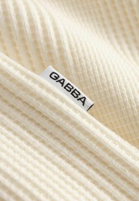 Krém színű bordás kötött anyag, amelybe egy kis fehér címke van varrva, rajta a "GABBA" felirattal.